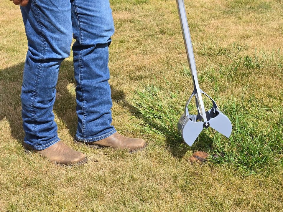 A crew member with a long-handled scooper on a lawn